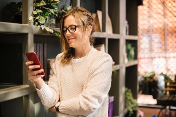 Frau mit Smartphone vor Bücherregal